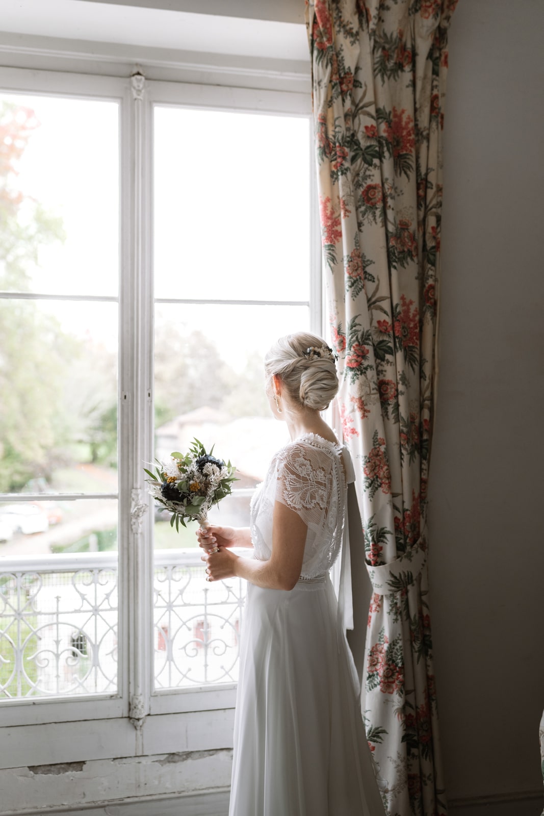 Préparatifs de la mariée qui regarde arriver son futur mari, bouquet à la main
